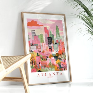 May include: A framed print of a colorful illustration of the Atlanta skyline. The print features a pink and orange sky with a white cloud, and the buildings are painted in various shades of pink, green, and blue. The text "ATLANTA GEORGIA" is printed in red at the bottom of the print.