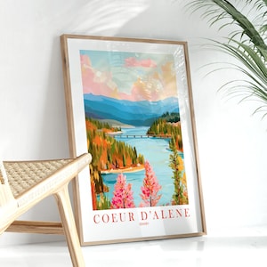 Puede incluir: Lámina artística enmarcada que representa un paisaje de Coeur d'Alene, Idaho. La obra muestra un lago con un puente, rodeado de árboles coloridos y montañas bajo un cielo vibrante. Las palabras "COEUR D'ALENE" están impresas en rojo en la parte inferior.