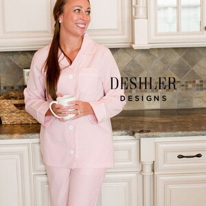 May include: Pink and white striped pajama set with white trim. The long-sleeved top has a button-down front and a breast pocket. The matching pants have a relaxed fit. The pajamas are from Deshler Designs.