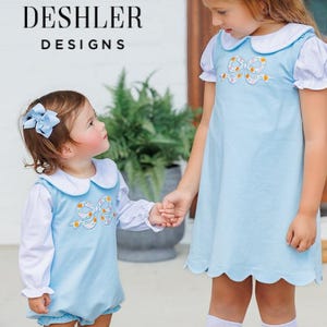 May include: A light blue jumper dress and a matching light blue bubble romper, both featuring white Peter Pan collars, white long sleeves, and an embroidered bow design on the chest. The text DESHLER DESIGNS is visible in the upper left corner.