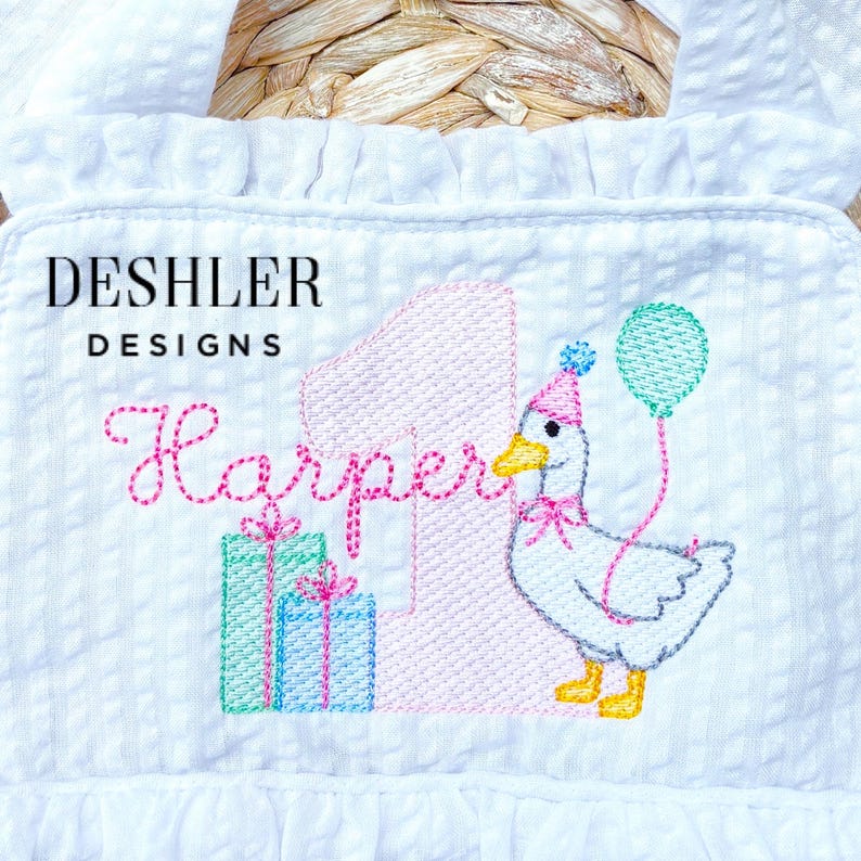 May include: White embroidered romper with a birthday theme. Features the text "DESHLER DESIGNS" and "Harper", a pink number 1, a goose wearing a party hat and holding a balloon, and two gift boxes. The romper has a ruffled trim.