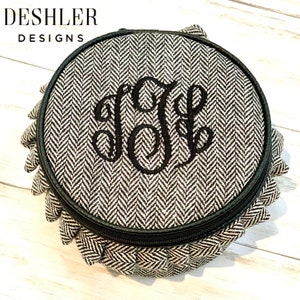 May include: A round, black and white, zippered jewelry organizer with a herringbone pattern and a monogrammed initial "J" in black thread.