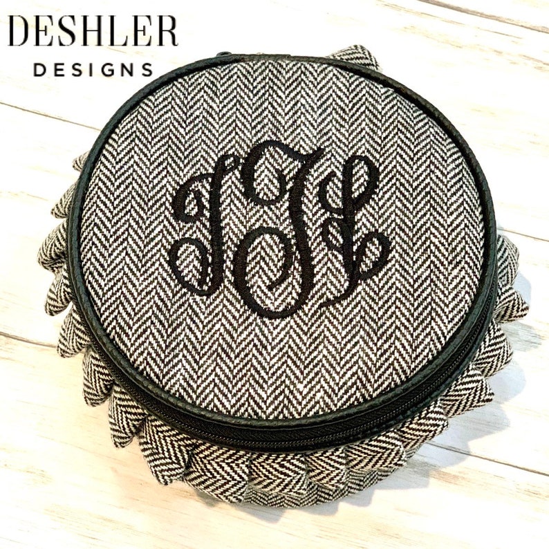 May include: A round, black and white, zippered jewelry organizer with a herringbone pattern and a monogrammed initial "J" in black thread.