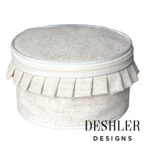 May include: A round, cream-colored linen storage box with a ruffled trim and a zipper closure. The box has a white label with the text "DESHLER DESIGNS".