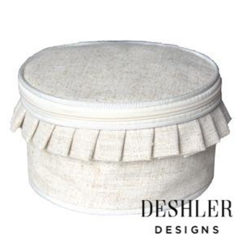 May include: A round, cream-colored linen storage box with a ruffled trim and a zipper closure. The box has a white label with the text "DESHLER DESIGNS".
