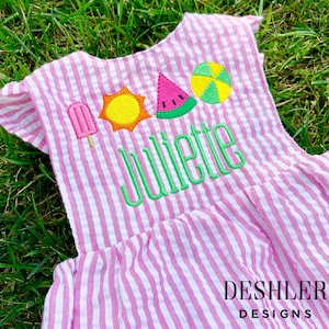May include: Pink and white striped dress with embroidered summer icons including a popsicle, sun, watermelon slice, and beach ball. The name "Juliette" is embroidered in green below the icons. "DESHLER DESIGNS" is embroidered in white at the bottom of the dress.