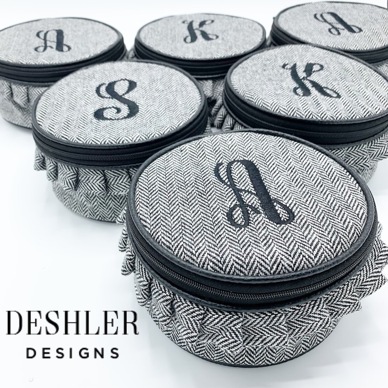 May include: Set of six round black and white patterned fabric storage boxes with black zipper closures and ruffled edges. Each box has a different letter monogrammed on the top in black thread. The boxes are arranged in a circle on a white surface. The text "DESHLER DESIGNS" is printed below the boxes.