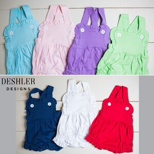 May include: A collection of baby rompers in various colors: light blue, pink, purple, green, navy blue, white, and red. Each romper features a ruffled bib, white buttons, and a gathered bottom. The brand name "DESHLER DESIGNS" is visible in the image.
