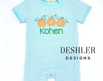 May include: A light blue and white striped baby onesie with a green vine and three orange pumpkins embroidered on the front. The onesie is personalized with the name "Kohn" in green embroidery. The text "DESHLER DESIGNS" is printed in black at the bottom of the onesie.