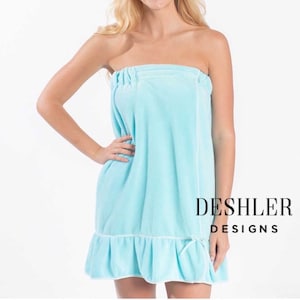 May include: A light blue terry cloth spa wrap with a ruffled hem and white trim. The wrap is strapless and has an elastic top. The text "DESHLER DESIGNS" is printed in black on the right side.