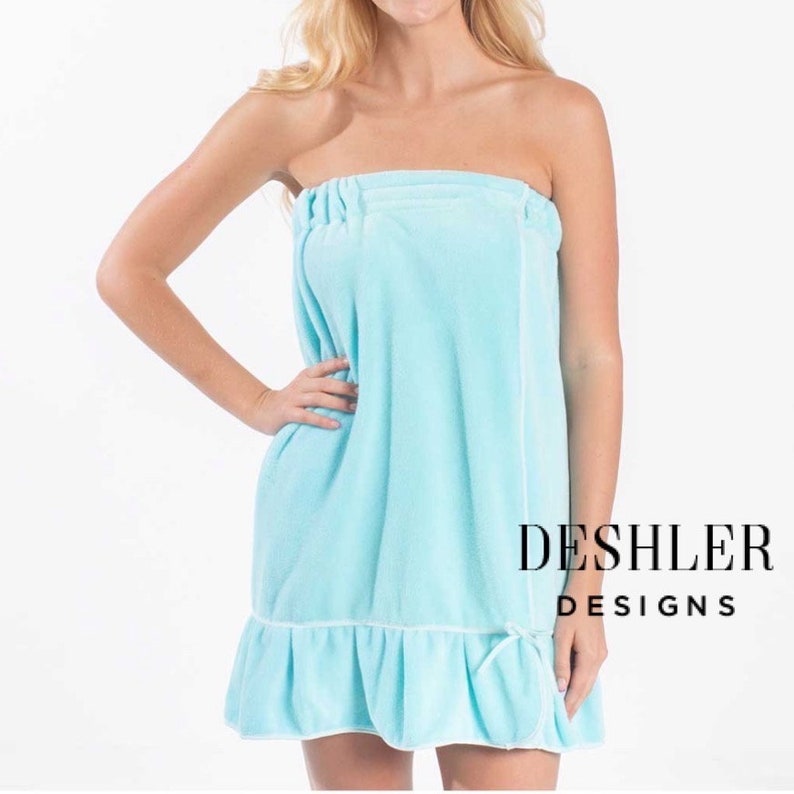 May include: A light blue terry cloth spa wrap with a ruffled hem and white trim. The wrap is strapless and has an elastic top. The text "DESHLER DESIGNS" is printed in black on the right side.