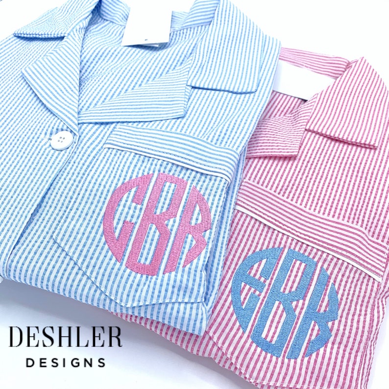 May include: Two seersucker pajama shirts, one light blue and one pink, with white stripes. Each shirt has a monogrammed pocket with the initials "GBB" in a contrasting color. The shirts have a classic button-down design and a collar.