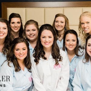 May include: A group of smiling people wearing light blue and white striped pajama shirts. One person wears a white pajama shirt with a pink monogram. The logo "DESHLER DESIGNS" is visible in the bottom left corner.