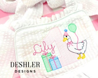 May include: A white seersucker romper featuring an embroidered design of a large pink number one, the name Lily in pink script, two gift boxes in green and blue, and a white goose wearing a pink party hat and holding a green balloon.