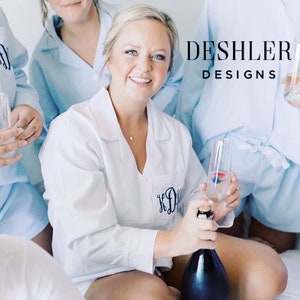 May include: White pajama shirt with a monogram and light blue pajama shorts. A woman is holding a champagne bottle and a glass of champagne. The text "DESHLER DESIGNS" is visible.
