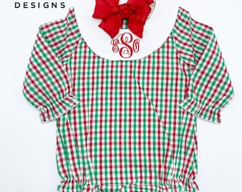 May include: A red and green gingham baby onesie with a white Peter Pan collar and a red bow. The onesie has a red embroidered monogram on the front.