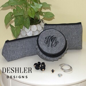 May include: Three gray and black zippered pouches with a herringbone pattern. The pouches are on a white surface with black beads, a ring, and two bracelets.