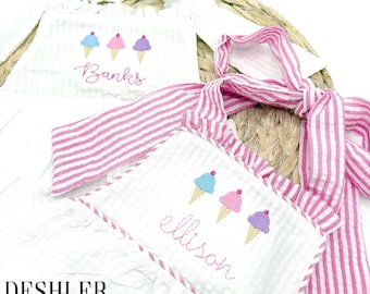 May include: Two white sleeveless dresses with pink and white striped straps. The dresses feature embroidered ice cream cones and the names "Banks" and "ellison".
