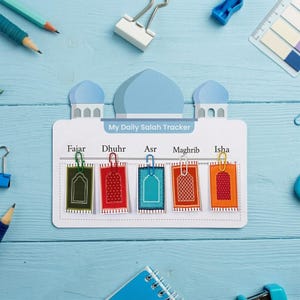 Può includere: Una scheda bianca My Daily Salah Tracker a forma di moschea con cupole blu. Riporta cinque nomi di preghiere: Fajar, Dhuhr, Asr, Maghrib e Isha. Ogni nome di preghiera ha un piccolo cartoncino rettangolare fissato con una graffetta.