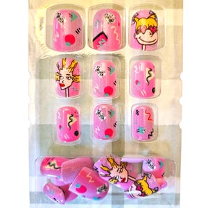 May include: A set of pink press-on nails with various designs. Some nails feature abstract shapes in teal, black, and red. Others showcase cartoon illustrations of a woman with heart-shaped glasses and a woman with yellow hair. The nails are packaged in a clear plastic container.