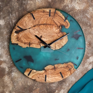 Puede incluir: Reloj de pared redondo con un diseño único. La esfera del reloj presenta un patrón de vetas de madera natural con un centro de resina turquesa. Las manecillas y los marcadores negros completan el diseño. El reloj mide aproximadamente 30 cm de diámetro.