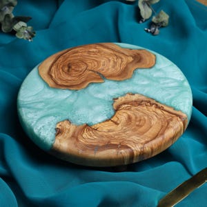 Peut inclure: Un plateau de service circulaire composé de deux morceaux de bois brun clair naturel aux motifs de grain prononcés, séparés par une incrustation de résine vert menthe translucide et tourbillonnante. Le plateau présente une finition lisse.