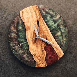 Peut inclure: Horloge murale ronde au design unique. Le cadran présente un centre en bois naturel avec une bordure en résine époxy rouge foncé et verte. Les aiguilles argentées complètent le design. Une pièce décorative pour n'importe quelle pièce.