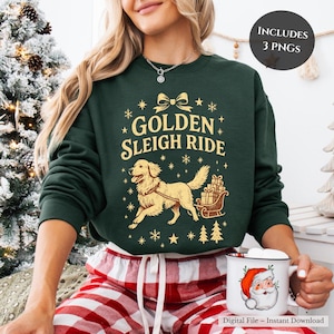 May include: A dark green sweatshirt with the words "GOLDEN SLEIGH RIDE" in gold lettering, featuring a golden retriever pulling a sleigh filled with gifts. The sweatshirt also has snowflakes and Christmas trees. A white mug with a Santa Claus graphic is also visible.