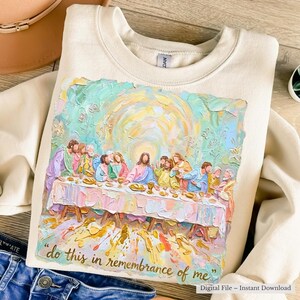 Puede incluir: Sudadera de color crema con una pintura texturizada y colorida de la &Uacute;ltima Cena. La obra de arte incluye figuras sentadas alrededor de una mesa, con la frase "do this in remembrance of me" debajo. La sudadera es un archivo digital.