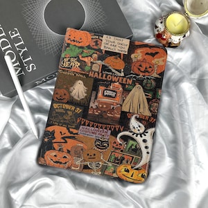 May include: A Halloween-themed tablet case featuring a collage of vintage-style illustrations. The design includes pumpkins, ghosts, and the text "October 31" and "Halloween". The case is rectangular and rests on a white, satin-like surface.