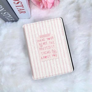 May include: A pink and white striped tablet case with the text "Make Your Heart The Prettiest Thing About You." The case has a black border and is on a white, fluffy surface.