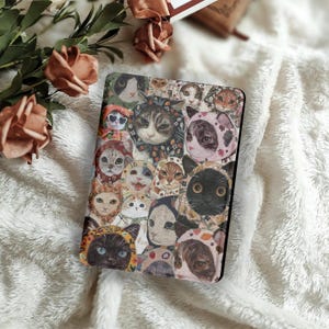 Op de afbeelding: Een rechthoekige hoes met een collage van kattenillustraties. De katten worden getoond in verschillende kostuums en uitdrukkingen, met een mix van kleuren en patronen. De hoes staat tegen een zachte, witte, getextureerde achtergrond met bloemaccenten.