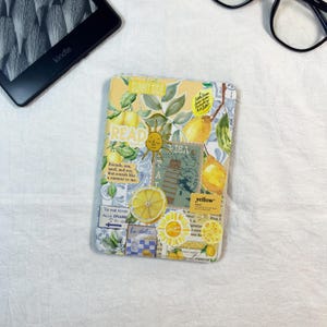Op de afbeelding: Een rechthoekige e-reader hoes met een collage van gele citroenen, groene bladeren, een zonne-illustratie en tekst waaronder "READ", "SUNNY SIDE", "yellow" en "la dolce vita". Het ontwerp bevat blauwe en witte tegelpatronen en vintage postzegels.