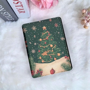 以下が含まれることがあります： クリスマスツリーのデザインが施された濃い緑色のタブレットケース。 金色のオーナメント、赤い装飾、星で飾られた木。 雪の結晶と雪に覆われた地面が、お祝いのシーンを完成させています。 ケースは白くふわふわした表面にあります。
