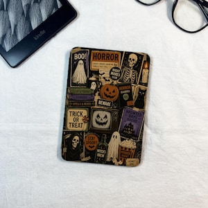 Puede incluir: Una funda rectangular para lector electrónico con un collage de ilustraciones de Halloween que incluye un fantasma, un esqueleto, una calabaza, un gato negro, la parca, un televisor con cara de calabaza y textos como Boo, Horror y Trick or Treat.