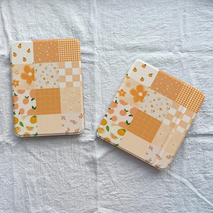 Peut inclure: Deux étuis pour tablette rectangulaires présentant un motif patchwork dans des tons orange, jaune et crème. Les motifs incluent de petites oranges, des carrés à carreaux, des fleurs, des pois et des lignes de grille.