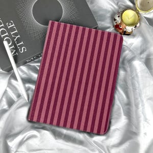 May include: A burgundy tablet case with vertical stripes. A white stylus and a book with the words "MODE STYLE" are visible. A decorative skull-shaped candle holder is also present.