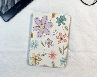 Puede incluir: Una funda blanca para Kindle adornada con un estampado floral en colores pastel. El diseño presenta varias flores en tonos morado, azul, rosa y amarillo, con hojas y tallos verdes. La funda es rectangular y está diseñada para un lector electrónico.