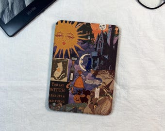 May include: A rectangular e-reader cover featuring a collage of illustrations including a large yellow sun, a dark house, a crescent moon, a black cat, a pumpkin, and a witch. The text reads, You say WITCH LIKE ITS A BAD THING.