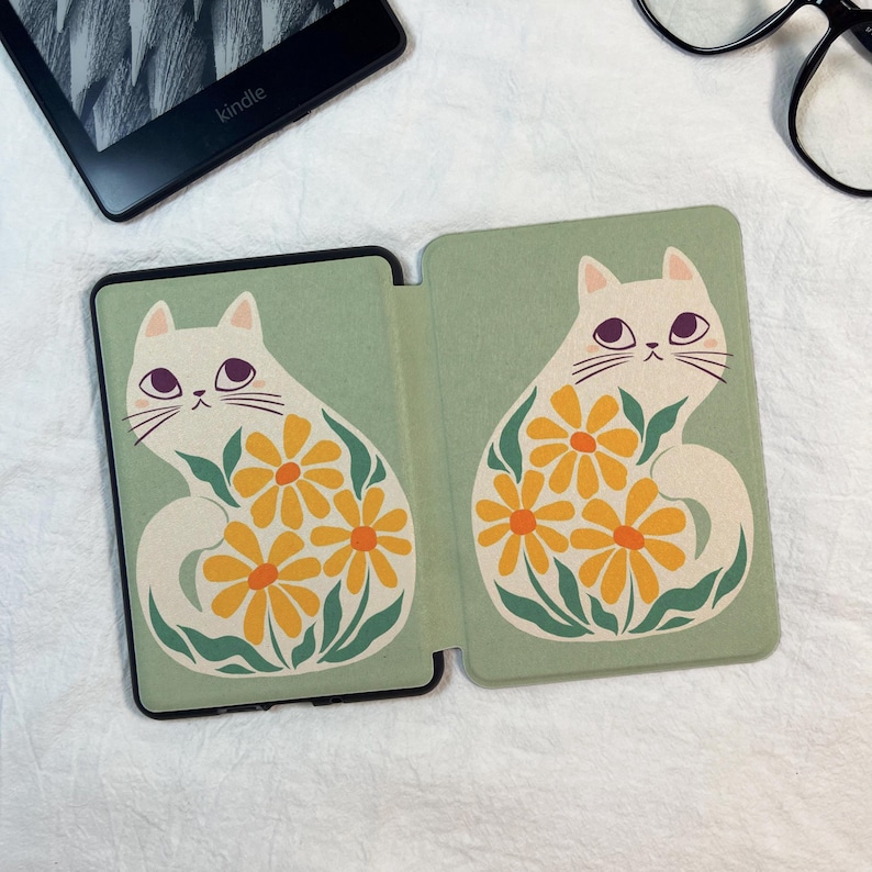 Pode incluir: Uma capa para leitor de e-books em verde s&aacute;lvia com uma ilustra&ccedil;&atilde;o repetida de um gato branco com olhos grandes e escuros, rodeado por margaridas amarelas e folhas verdes. O design cobre ambos os pain&eacute;is da capa protetora dobr&aacute;vel.