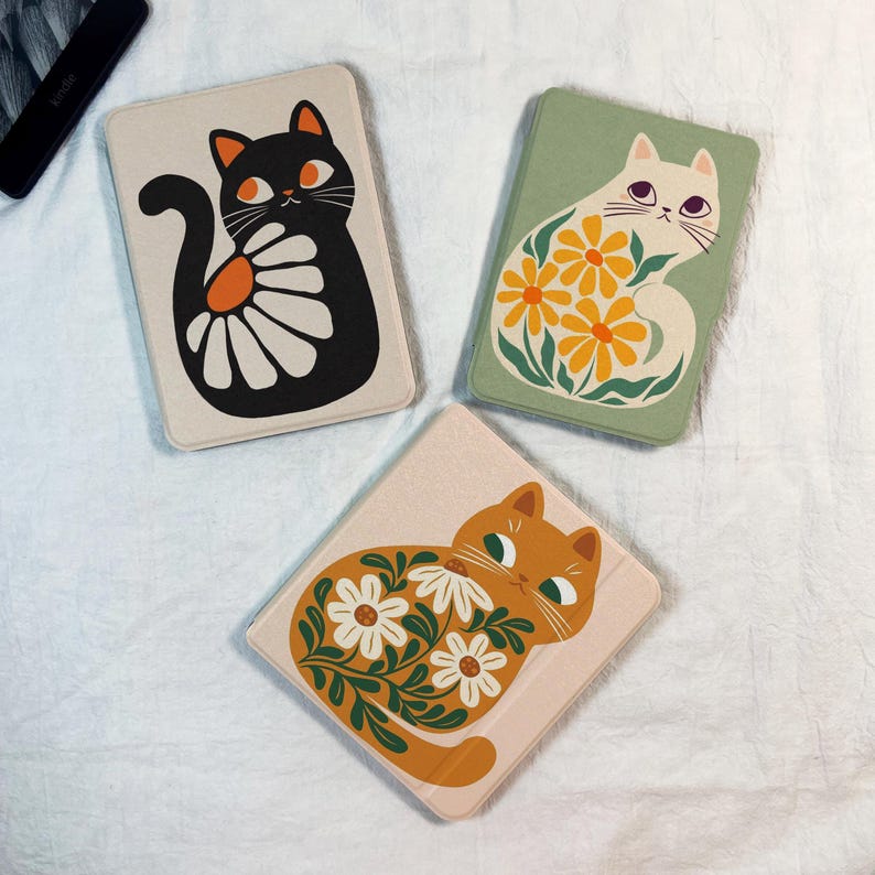 Pode incluir: Tr&ecirc;s capas retangulares para e-reader com ilustra&ccedil;&otilde;es de gatos. Uma capa creme com um gato preto e uma margarida branca, uma verde s&aacute;lvia com um gato branco e flores amarelas, e uma rosa claro com um gato laranja e flores brancas.
