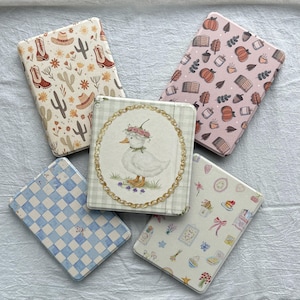 May include: Five decorative boxes with various designs. One box features a duck wearing a floral crown, another has a cowboy theme, and a third has a blue and white checkered pattern. The other two boxes have a fall theme and a floral design.