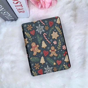 Puede incluir: Una funda de tableta gris oscuro con un patrón navideño festivo. El diseño incluye hombres de jengibre, copos de nieve, bastones de caramelo, corazones y estrellas. La funda está decorada con detalles dorados, rojos y blancos.