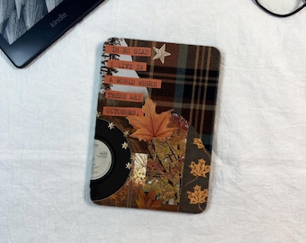 Può includere: Una skin rettangolare per e-reader con un design a collage che presenta un motivo scozzese marrone, un disco in vinile nero e foglie d'acero autunnali. Il testo recita: I'M SO GLAD I LIVE IN A WORLD WHERE THERE ARE OCTOBERS. Finitura opaca.