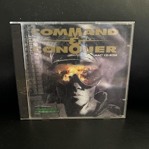 May include: A CD-ROM case for the video game "Command & Conquer" featuring a soldier with a fiery background. The game title is in gold lettering. The case is clear plastic with the Westwood Studios logo.