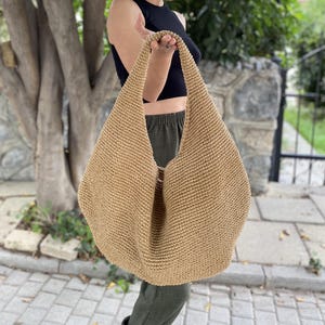 May include: A large, tan, crocheted tote bag with a wide, open top and a single, long handle.