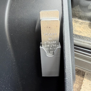 May include: A gray 3D-printed holder with two metal tools. The tools have text that includes "443626" and "SERIAL #". The holder is mounted inside a vehicle's console.