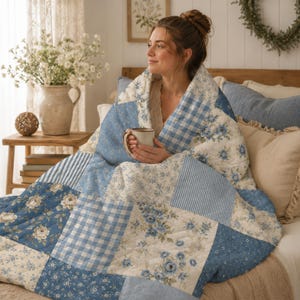 May include: A patchwork quilt featuring a variety of blue and white fabric squares. The design includes alternating patterns of floral prints, blue and white gingham checks, and thin vertical stripes, all stitched together in a quilted texture.