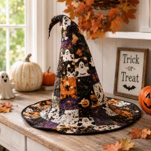May include: A tall, pointed witch hat constructed from a patchwork of quilted fabric featuring black, orange, and purple patterns with printed ghosts and jack-o'-lanterns. The hat has a wide, circular brim and a slightly curved, drooping tip.