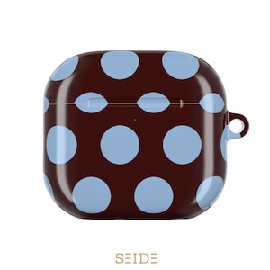 May include: A brown AirPod case with a light blue polka dot pattern. The case has a rounded square shape with a small loop on the side. The brand name "SEIDE" is printed at the bottom.